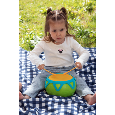 Criança a tocar tambor verde com pele laranja num cobertor azul e branco