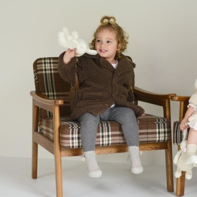 Criança com casaco felpudo castanho sentada em cadeira de madeira com almofadas xadrez