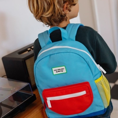 Mochila infantil azul, vermelho e amarelo com etiqueta, vista de costas num menino