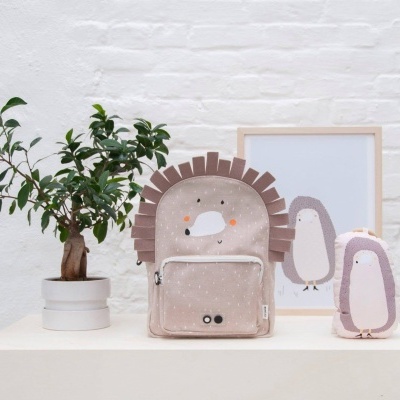 mochila infantil rosa claro com design de porco-espinho, bolso frontal, chaleira e quadro com ilustração de pinguim sobre mesa branca