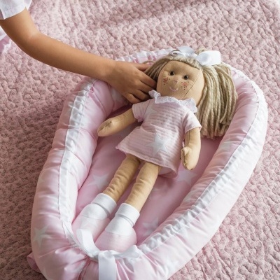 Boneca de tecido rosa num suporte acolchoado cor-de-rosa sobre manta rosa acolchoada