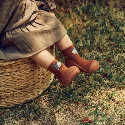 Botas castanhas para bebé com meias decoradas com raposas sentada numa cesta de palha