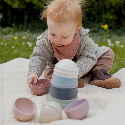 Criança a brincar com copos empilháveis de plástico em tons pastel num cobertor ao ar livre
