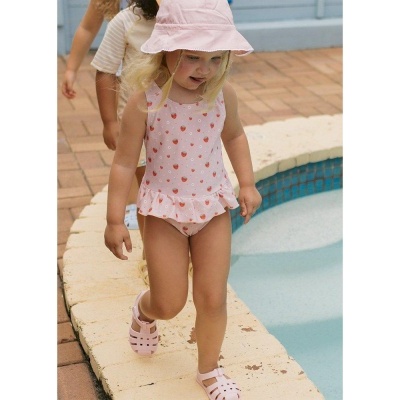 Criança com fato de banho rosa e chapéu junto a piscina