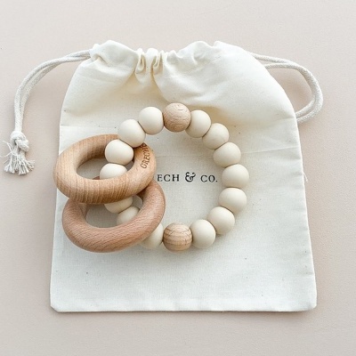 Brinquedo para bebés com anéis de madeira e contas de silicone em saco branco.