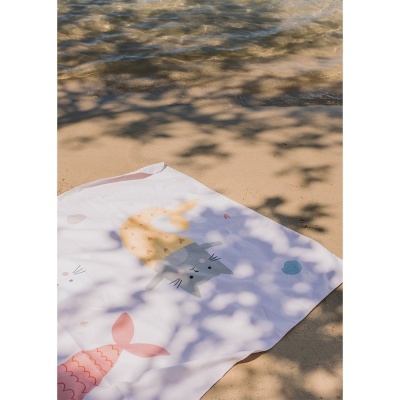 Paninho branco com desenhos de gatinhos sereias sobre areia e sombra de folhas