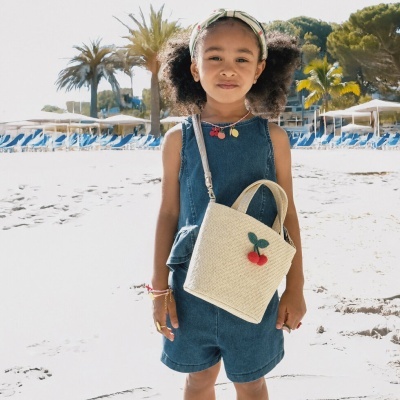 Menina na praia com vestido azul e bolsa creme com cerejas