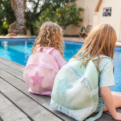 Duas meninas sentadas junto a piscina com mochilas rosa e verde com estrelas