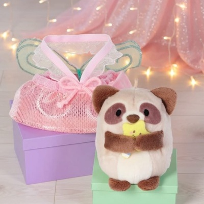 Pelúcia de animal segurando brinquedo em caixa verde ao lado de caixa roxa com saco rosa e asas decorativas