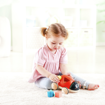 Menina pequena a brincar com brinquedo de madeira vermelho em forma de carrinho no tapete