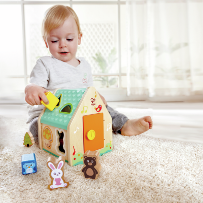 Criança a brincar com casinha de madeira e figuras de animais coloridas num tapete claro