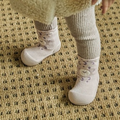 Meias-calçado creme com padrão de onça usadas por bebé sobre tapete bege