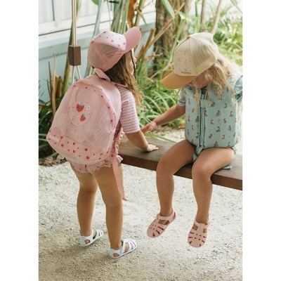 Crianças com mochilas coloridas e bonés, sandálias, ambiente ao ar livre