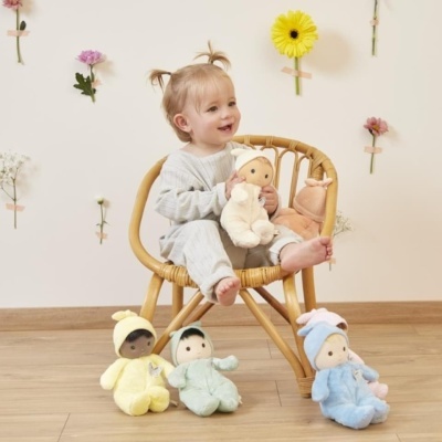 Criança sentada numa cadeira rattan com boneca de peluche e outras três bonecas no chão