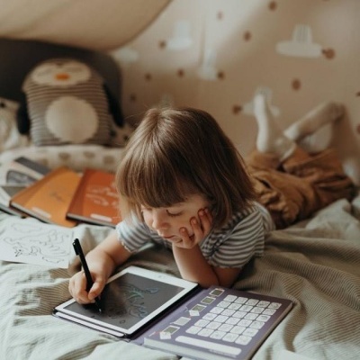 Criança a desenhar numa tablet num quarto infantil com almofada de pinguim e parede decorada