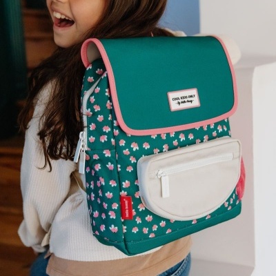 Mochila verde com flores cor-de-rosa e bolso bege, usada por criança sorridente
