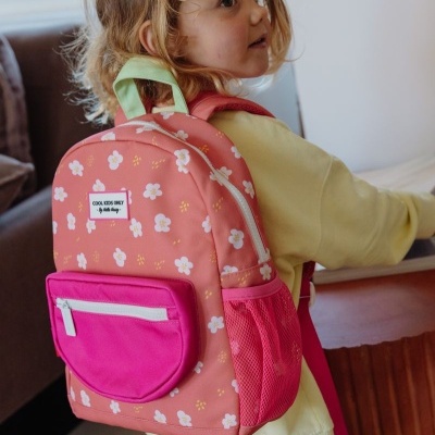 Mochila infantil rosa com flores brancas e bolso rosa forte vista de lado com criança a usá-la.