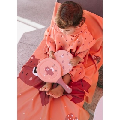 Criança com poncho e raquetes de praia laranja com desenhos de ursinho e cogumelos