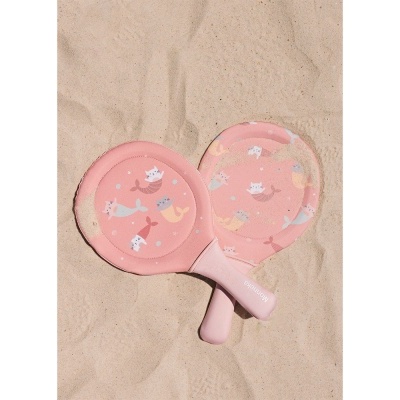 Duas raquetes de praia cor-de-rosa com padrão de gatos sereia sobre areia.