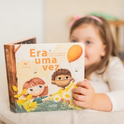Criança deitada segurando um livro infantil intitulado Era uma vez com ilustrações coloridas