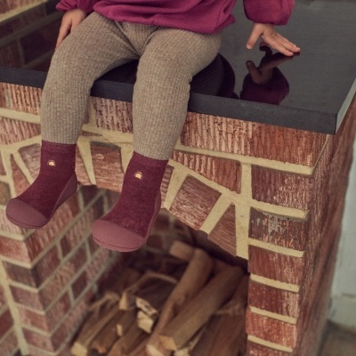 meias castanho vermelho com antiderrapante usadas por criança sentada numa lareira de tijolos vermelhos