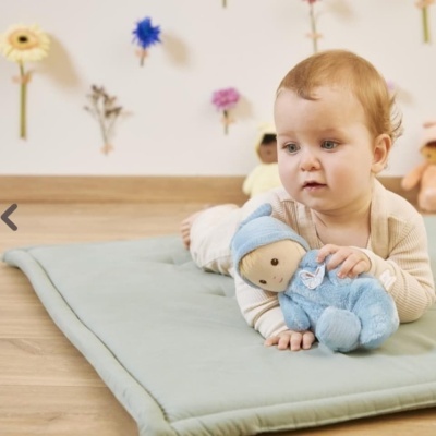 Criança deitada em almofada verde clara, segurando boneco azul de pelúcia