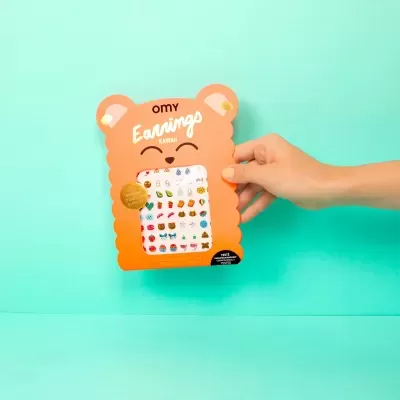 Embalagem laranja em forma de urso com brincos adesivos coloridos em fundo azul claro