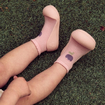pés de criança com meias cor-de-rosa decoradas com uvas e sapatos de borracha rosa claro na relva