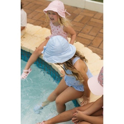 Crianças sentadas à beira de piscina com chapéus e fatos de banho coloridos