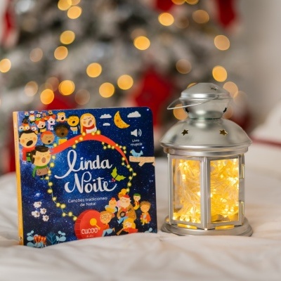 Livro infantil 'Linda Noite' ao lado de lanterna iluminada num cenário de Natal