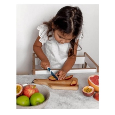 Menina pequena a cortar maçã vermelha num tabuleiro de madeira na cozinha