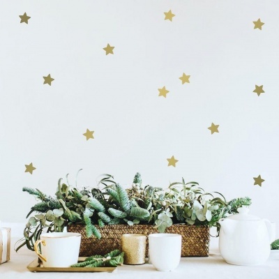 Mesa com arranjo de plantas verdes e brunch branco, jarro branco e decoração de estrelas douradas na parede