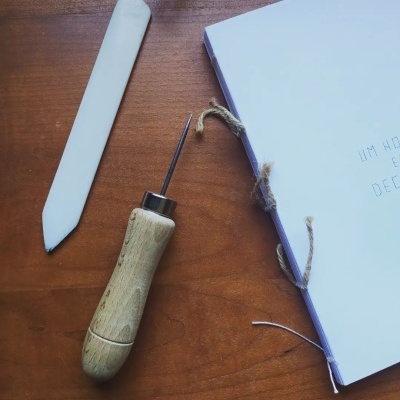 ferramenta de cabo de madeira, régua branca e caderno com capa branca amarrado com corda sobre mesa de madeira