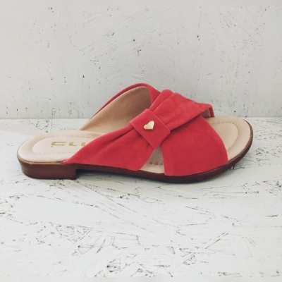 Chinelo vermelho com laço e coração dourado sobre superfície branca