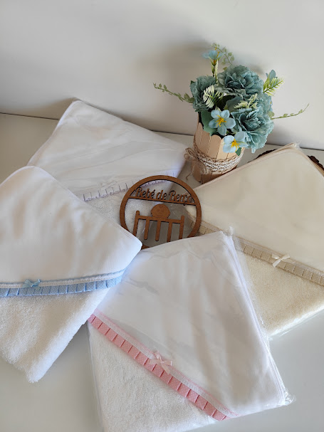 Toalhas brancas com bordado azul e rosa, placa de madeira redonda e vaso com flores azuis e verdes