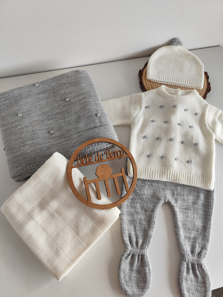 Conjunto de roupa de bebé em cinzento e branco com gorro, casaco, calças, mantas e placa de madeira