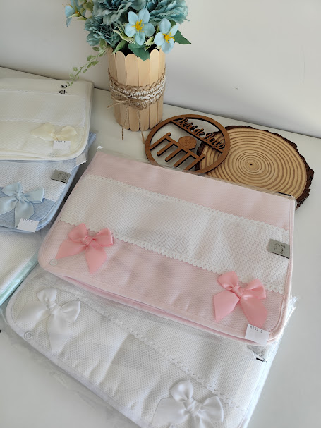 Mantas decoradas com laços em rosa e branco, com vaso de flores e decoração em madeira ao fundo