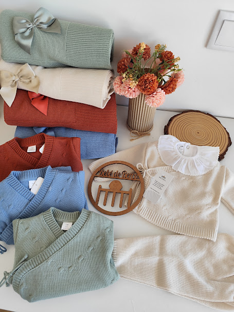 Roupas de bebé em malha coloridas organizadas com flores e decoração em madeira