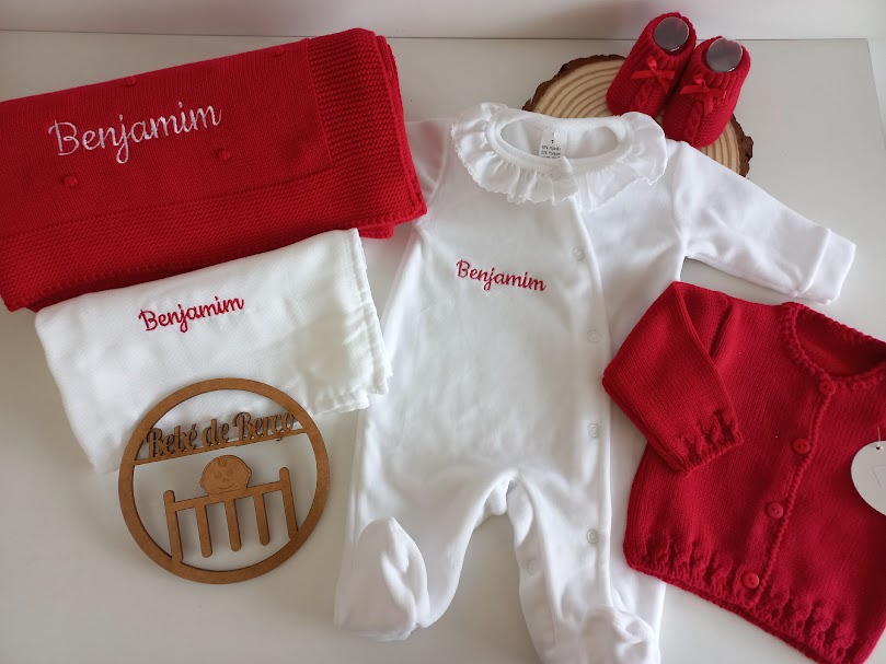 Conjunto de roupa de bebé com manta, macacão, casaco e botas vermelhas e brancas, nomes bordados e suporte de madeira com texto