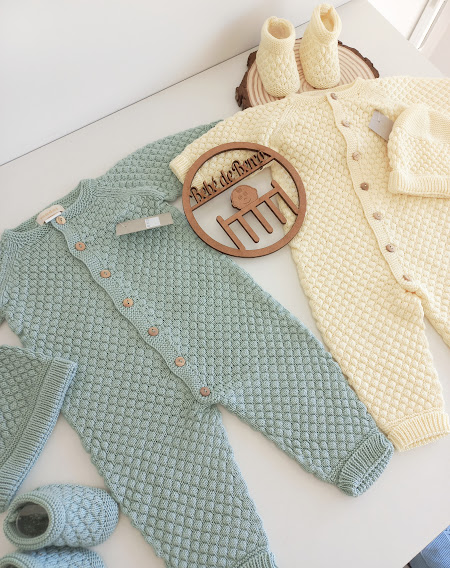 Dois macacões de bebé verde claro e creme com botões, botas e gorros correspondentes, junto a emblema de madeira com texto Babyluce.