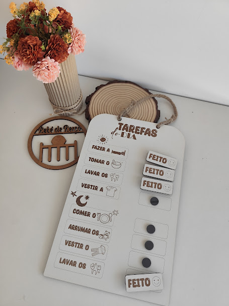 Quadro branco de tarefas diárias com texto em português, ícones e legendas móveis, jarro com flores coloridas ao lado, superfície branca.