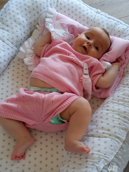 Bebé a deitar-se em almofada acolchoada com conjunto de malha rosa.