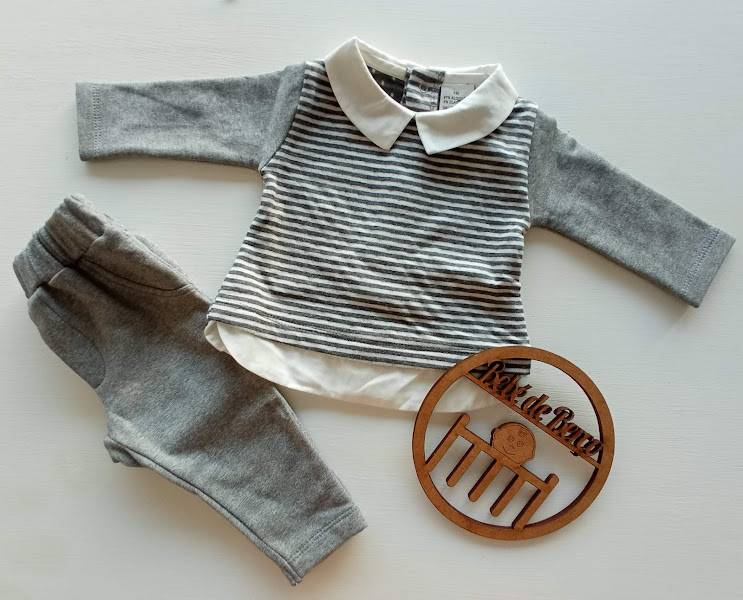Conjunto de roupa para bebé com camisola às riscas e calças cinzentas junto a objeto decorativo redondo em madeira