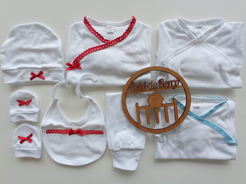 Conjunto branco de roupa de bebé com detalhes vermelhos e azuis e acessório de madeira redondo