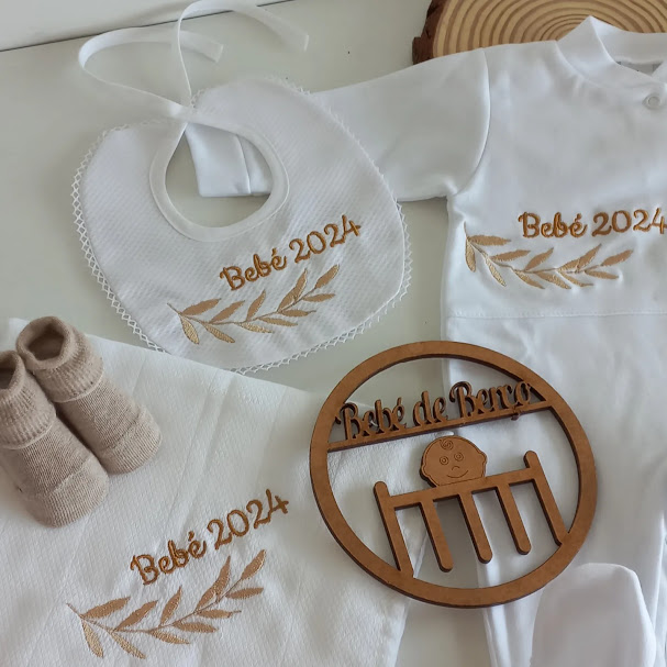 Conjunto de roupa de bebé branco com bordados castanhos e ornamento de madeira