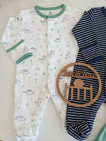 Dois macacões de bebé, um branco com dinossauros e outro azul com riscas brancas