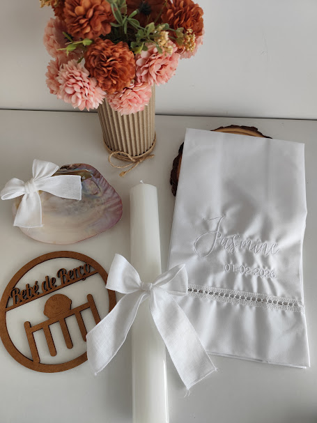 Vela, toalha bordada, concha, placa de madeira e vaso com flores