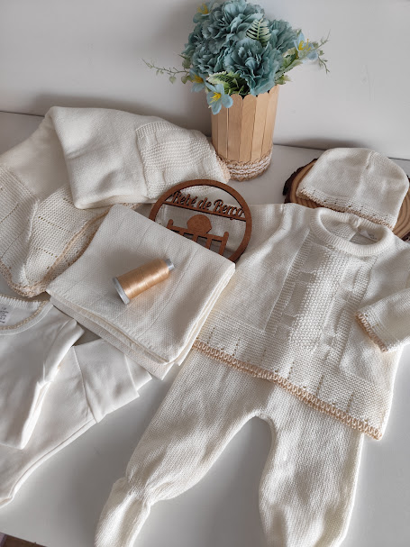 Conjunto de roupa de bebé branco com detalhes bege e vaso de flores azuis