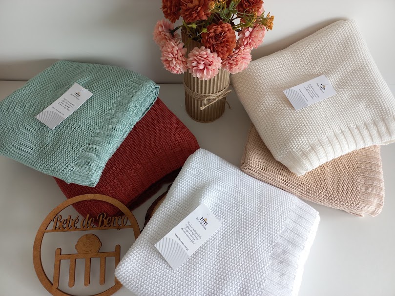 Cinco mantas coloridas com etiquetas e um vaso com flores sobre uma superfície branca