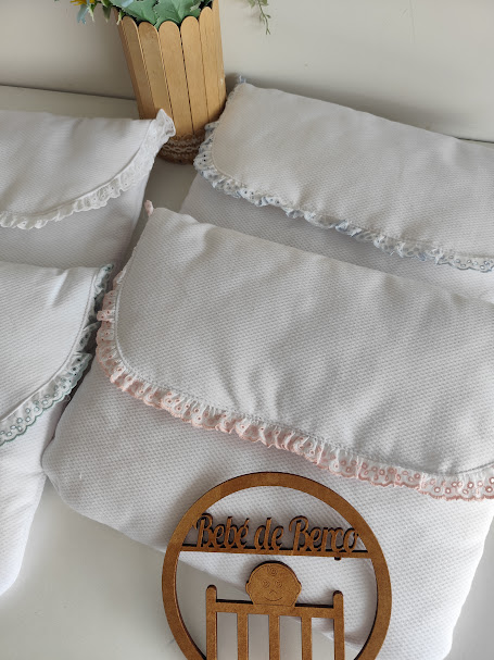 Três almofadas brancas com bordas em renda de cores diferentes e enfeite de madeira Bebé de Berço